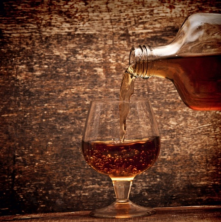 Cognac pour from a bottle in a glass on wood backgroundの写真素材