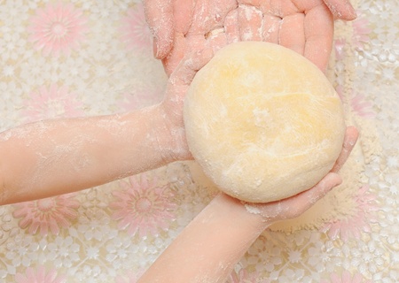 A child is helping mom to knead the dough for baking 