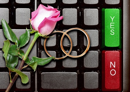 Wedding rings and red roses on computer keyboard. answer from a marry proposal の写真素材