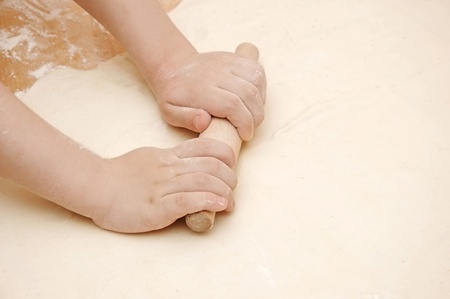 Child's hands roll out the dough on wooden table