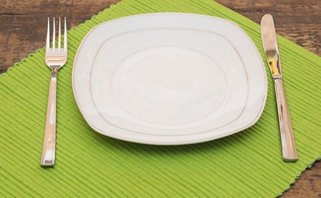 Empty dish, knife and fork and green napkin on wood table の写真素材