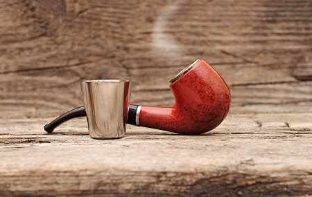 stainless glass of cognac and tobacco pipe on old wooden background. 