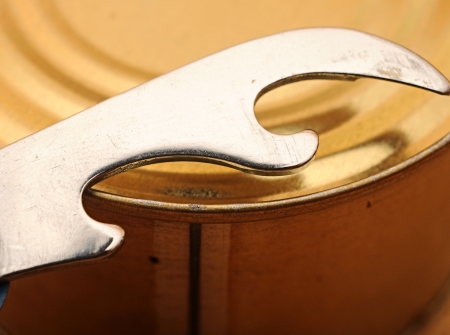 close-up old tin opener opening a can on wooden table