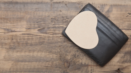 Black leather purse with paper heart on wooden background