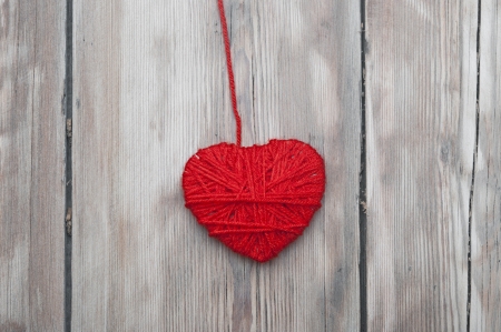 a heart made of red wool yarn hanging on old wood . の写真素材