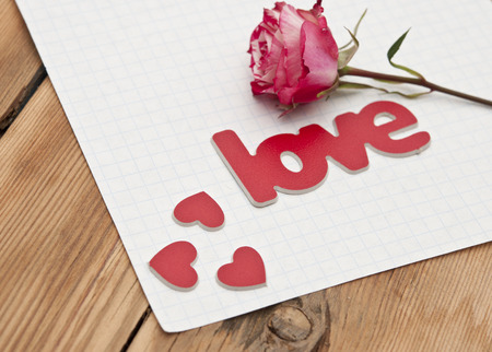 red-white rose and scattered flower petals and the word love on a rustic background  の写真素材