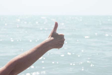 Woman's hand showing thumbs up or shows good and like on the beach against blue sea background.の写真素材