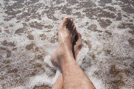 Male feet on a pebble beach and sea waves at sunsetの写真素材