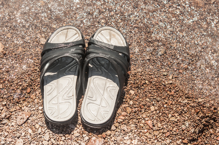 Black slippers on the sand beach with relaxing wavesの写真素材