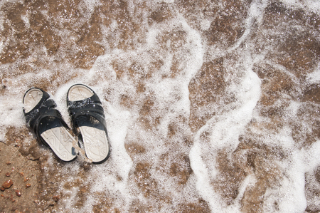Black slippers on the sand beach with relaxing wavesの写真素材