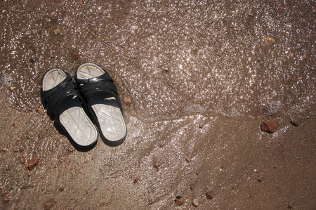 Black slippers on the sand beach with relaxing wavesの写真素材