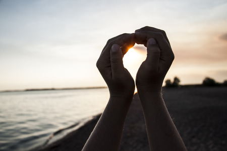Silhouette hand in heart shape with sunrise in the middle and beach backgroundの写真素材