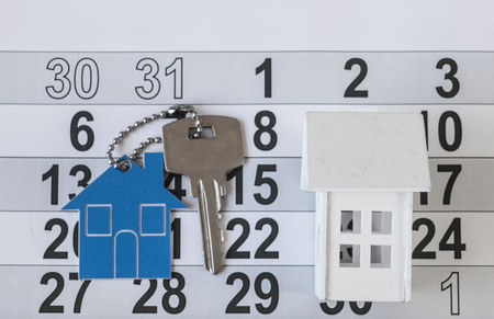 House key on a house shaped keychain resting on calendar background. Concept for real estate, moving home or renting propertyの写真素材