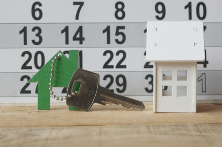 House key on a house shaped keychain resting on calendar background. Concept for real estate, moving home or renting propertyの写真素材
