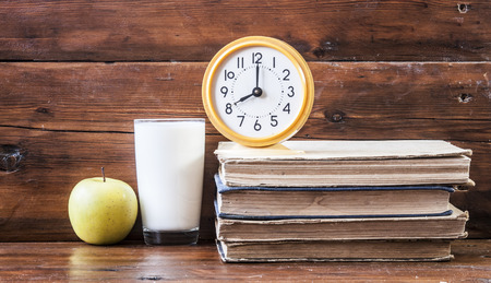 glass of fresh milk with green apple on wooden table with booksの写真素材