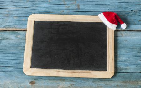 Blackboard with santa claus hat on white wood on rustic wooden background with copy space for textの写真素材