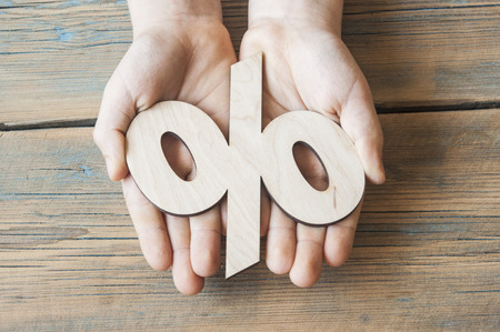 kid hands holding red percentage sign on wooden background.の写真素材