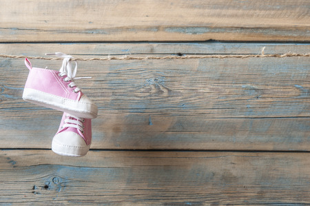 Baby shoes hanging on the colorful clothesline over wooden backgroundの写真素材