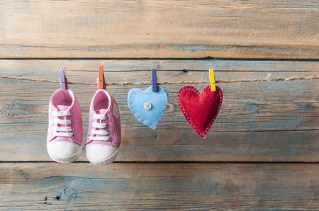 Baby shoes hanging on the colorful clothesline over wooden backgroundの写真素材