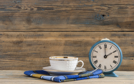 Tea or coffee cup and alarm clock on wooden table.