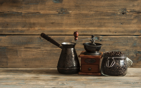 Roasted coffee beans in glass jar, coffee grinder and jezva on wood tableの写真素材