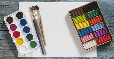 Set of watercolor paints, brushes for painting with colorful plasticine and blank white paper sheet on vintage wooden background. Top view.の写真素材