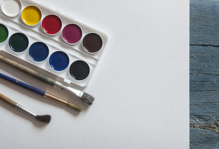 Set of watercolor paints, brushes for painting and blank white paper sheet on vintage wooden background. Top view.の写真素材