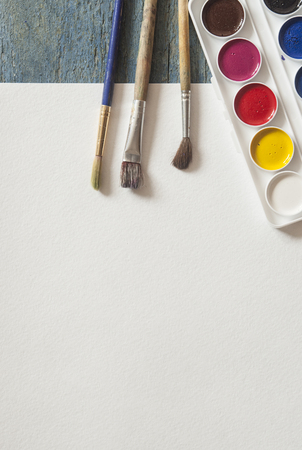 Set of watercolor paints, brushes for painting and blank white paper sheet on vintage wooden background. Top view.の写真素材