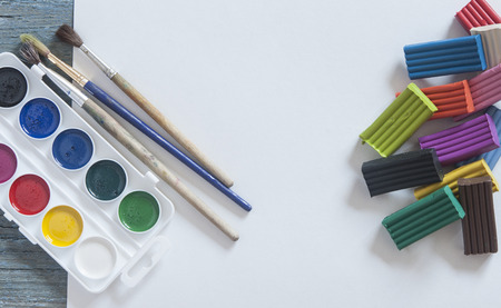 Set of watercolor paints, brushes for painting with colorful plasticine and blank white paper sheet...