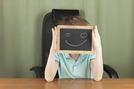 Young boy hiding his face with a small blackboard with a smiley face on itの写真素材
