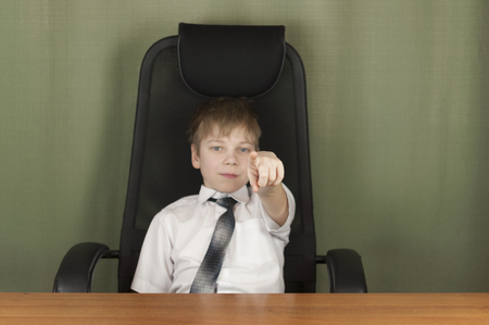 Portrait of stylish business child sitting at workplace. Cute caucasian boy imitating businessperson or office workeの写真素材