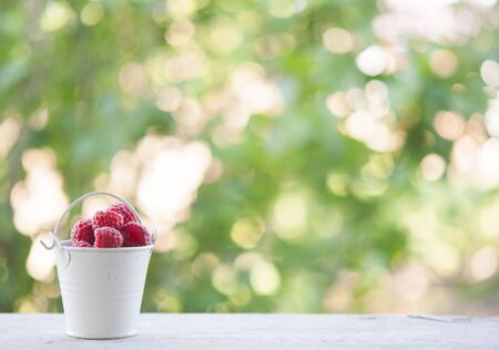 Sunlit small bucket of fresh strawberries on outside table with summer foliage in background.の写真素材