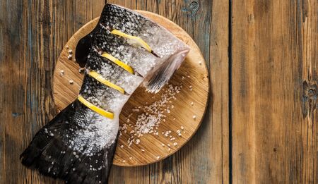 raw salmon red fish tail with lemon and sea salt on a cutting kitchen board surfaceの写真素材