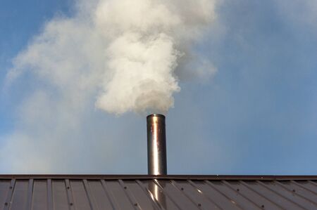 Chimney made of iron. Smoke from the chimney, heating. smoke billowing. coming out of a house chimney against a blue sky backgroundの写真素材