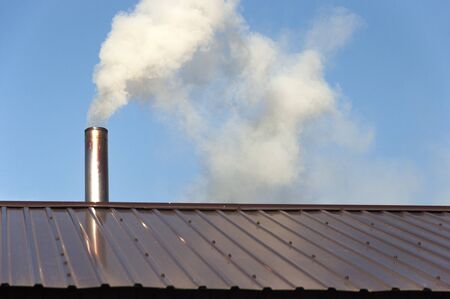 Chimney made of iron. Smoke from the chimney, heating. smoke billowing. coming out of a house chimney against a blue sky backgroundの写真素材