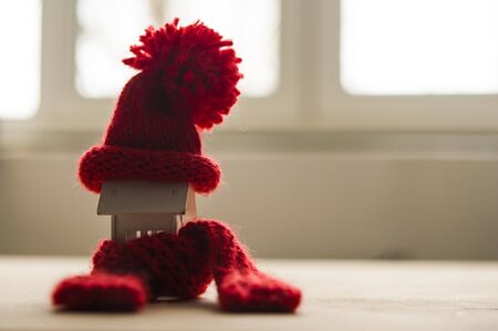 House model with knitted hat and scarf on table against white background. Heating concept