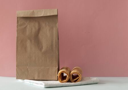 brown paper bag with wafer roll cookies over soft pink backgroundの写真素材
