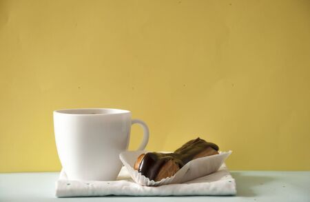 white coffee cup with chocolate cookies over yellow background