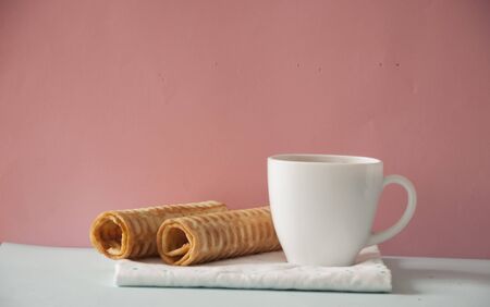 white coffee cup with empty wafer tubes over soft pink backgroundの写真素材