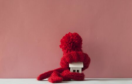House model with knitted hat and scarf on table against pink background. Heating conceptの写真素材