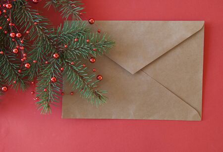 Christmas and New Year background with fir branches and brown envelope on red paper background. ...