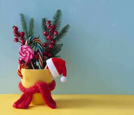 Christmas or new year card. Christmas candy canes in yellow mug with berries holly branches and Christmas decoration.の写真素材