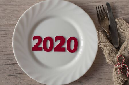 2020 New year concept on empty white plate, fork and knife on wooden tabletop. Top view, copy space, Table setting. background for menu, layoutの写真素材
