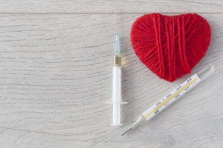 An old mercury thermometer with syringe and red heart on wood background. Medical health care. Top viewの写真素材