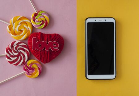 Valentine's day, blank screen smartphone on pink background with red heart and lollipop, love and connection between them, romantic picture, suitable for advertisingの写真素材