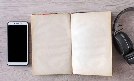 headphones, smartphone and open blank book on wooden table. Top view. audiobook. hobby. free time....