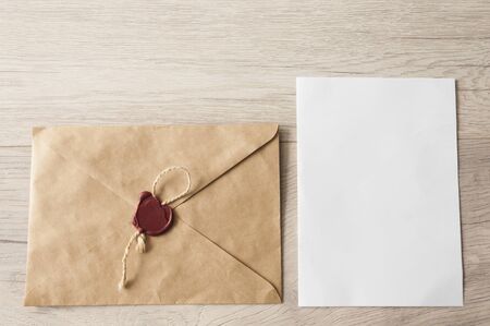 Blank envelope with white blank paper inserted into it on light wood table background. View from...