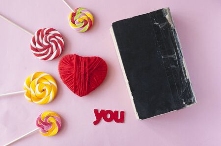 red heart, old closed book and lollipop on a pink background. Top viewの写真素材