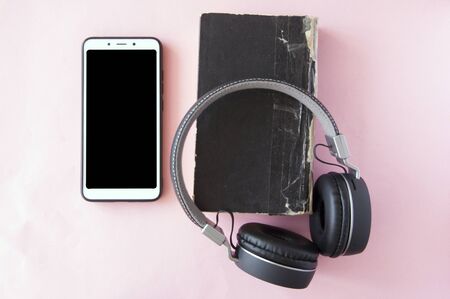 headphones, smartphone and old book on pink paper background. Top view. audiobook. hobby. free time. recreation. literature.の写真素材