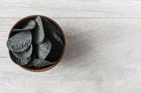 black potato chips in wooden bowl on wooden table. Top viewの写真素材